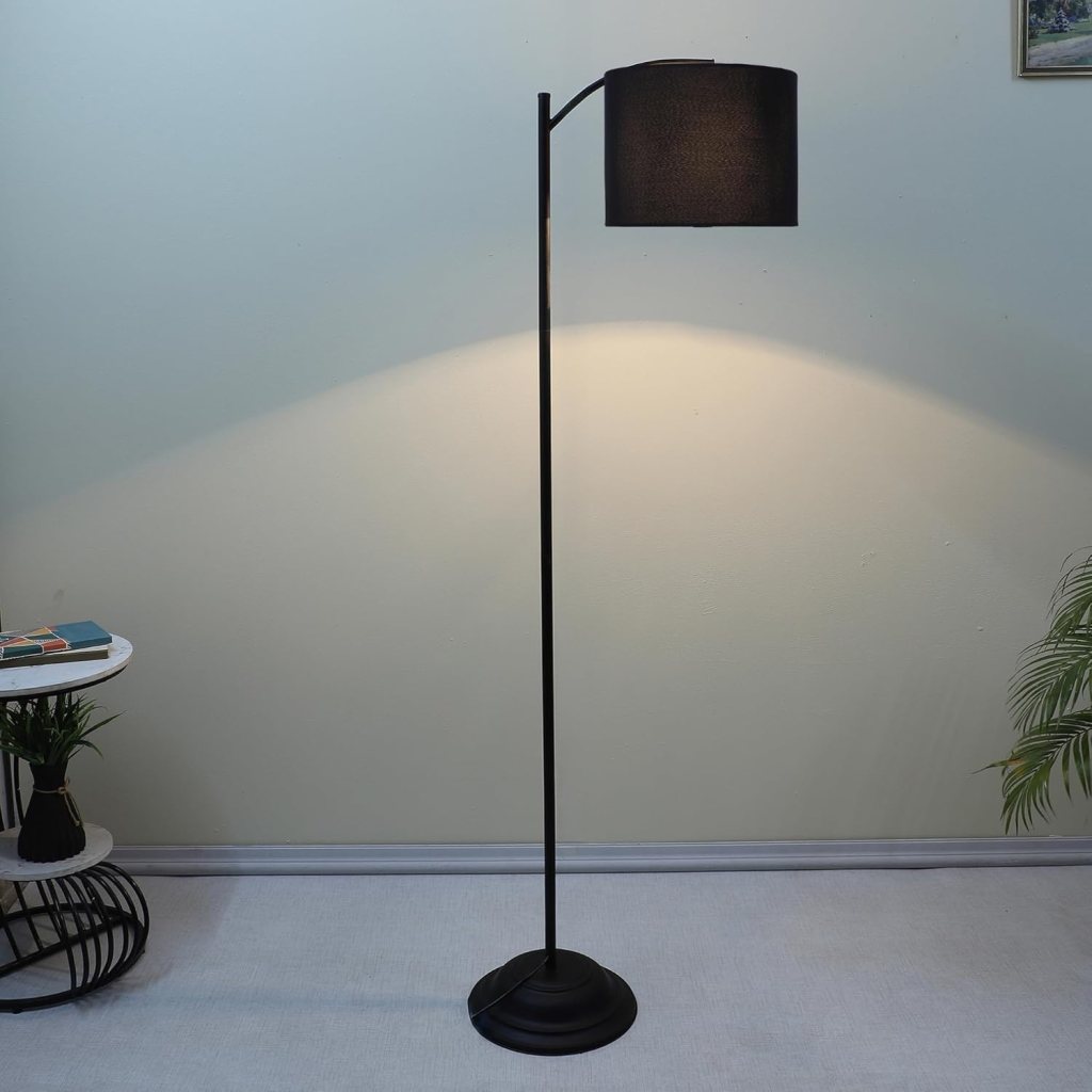 A modern black floor lamp with a cylindrical shade, casting warm light in a softly decorated room.